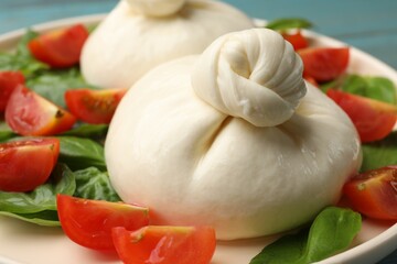 Delicious burrata cheese with tomatoes and basil on table, closeup