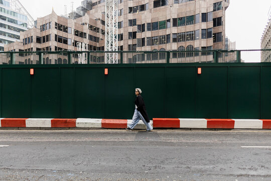 Modern woman walking by urban construction fence on city street