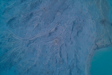 Aerial top down view of grey industrial sludge with flow channels and cyan water. Toxic waste texture and surreal pollution landscape background.