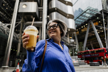 Smiling woman enjoying smoothie outdoors in urban London setting