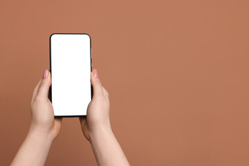 Woman holding smartphone with blank screen on brown background, closeup. Mockup for design