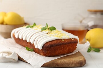 Tasty lemon cake decorated with icing, zest and mint served on white tiled table, closeup
