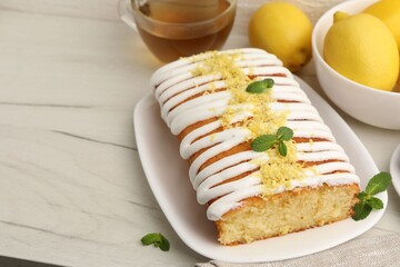 Tasty lemon cake decorated with icing, zest and mint served on white table, closeup. Space for text