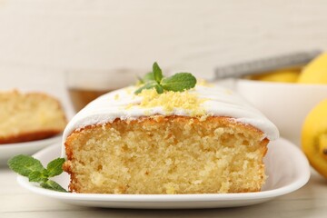 Tasty lemon cake decorated with icing, zest and mint served on white table, closeup
