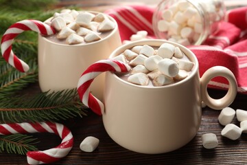 Tasty cocoa with marshmallows, candy canes and Christmas decor on wooden table, closeup