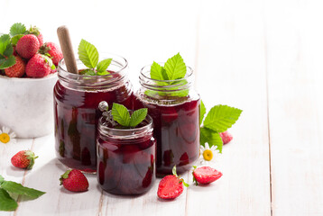 Three jars of strawberry jam with fresh strawberries on the table, close-up