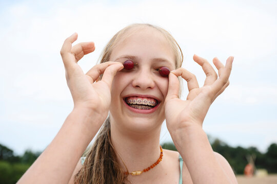 Smiling youth with dental braces playing with berries outdoors in summer