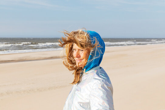 Red haired woman smiling in wind on beach near North Sea