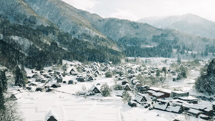 Panoramic aerial view of the historic Shirakawa-go village in Japan, featuring Gasshō-zukuri houses covered in snow amidst mountains