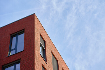 Modern brick building corner with large windows and exterior blinds under blue sky. Concept of urban architecture, commercial property and contemporary exterior design.