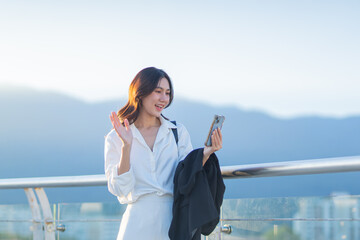Confident Asian businesswoman smiling in a modern corporate setting, attractive professional lady standing outdoors, showcasing success, beauty, career ambition, and cheerful lifestyle.
