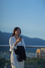 Confident Asian businesswoman smiling in a modern corporate setting, attractive professional lady standing outdoors, showcasing success, beauty, career ambition, and cheerful lifestyle.