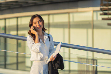 Confident Asian businesswoman smiling in a modern corporate setting, attractive professional lady standing outdoors, showcasing success, beauty, career ambition, and cheerful lifestyle.