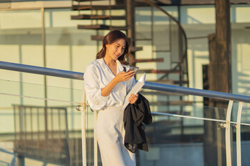 Confident Asian businesswoman smiling in a modern corporate setting, attractive professional lady standing outdoors, showcasing success, beauty, career ambition, and cheerful lifestyle.