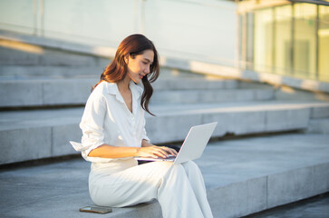 Confident Asian businesswoman smiling in a modern corporate setting, attractive professional lady standing outdoors, showcasing success, beauty, career ambition, and cheerful lifestyle.
