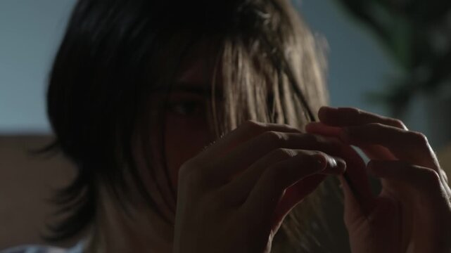 Mental illness alone reflected in young man quietly twisting strand of hair in anxious focus. Person isolating in dim room showing signs of emotional tension and inner struggle. Teenager fidgeting