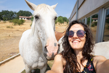 Woman taking a selfie with white horse in paddock