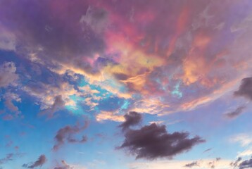 A dramatic sky filled with nacreous clouds displaying rainbow iridescent colors mixed with dark storm clouds during sunset or sunrise.