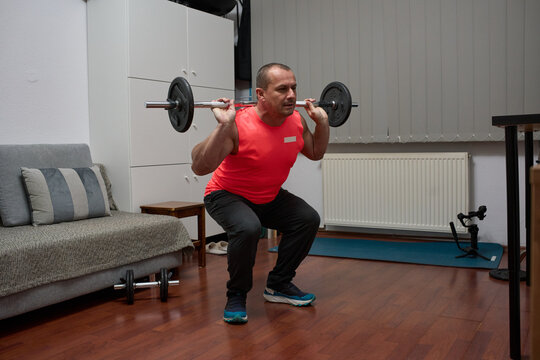 Man doing barbell squats at home - Powered by Adobe