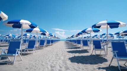 Lines of blue and white striped umbrellas and blue beach chairs on sandy beach under clear blue sky, summer vacation concept.