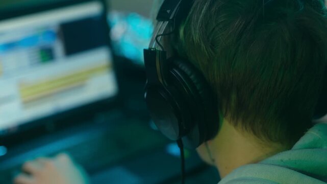 Rear View Person With Headphones At Laptop, Focused Audio Editing Session Using Timeline And Software, Hands On Keyboard With Glowing Monitor And Led Backlight, Producer Workflow And Content