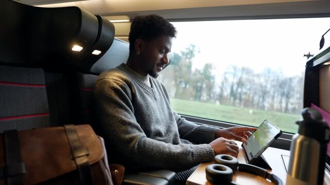 Black male commuter working on tablet computer traveling by train