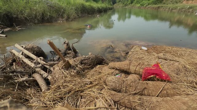 Leftover festival straw and broken idol materials pile up along the riverbank, clogging the shallow water and highlighting severe environmental pollution.