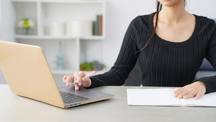 部屋でノートパソコンを見ながら勉強する女性