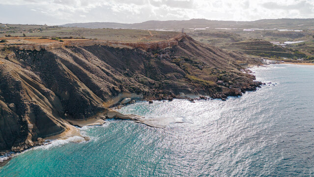 Malta's scenic coastline at Ajn Tuffieha with turquoise water, rocky cliffs, and a sandy beach. - Powered by Adobe