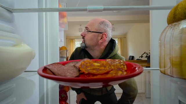 Man opening fridge, finding spoiled sausage and tossing it back with disgusted expression, view from inside of fridge. Male realizing food is rotten while feeling grossed out and annoyed. Guy throwing