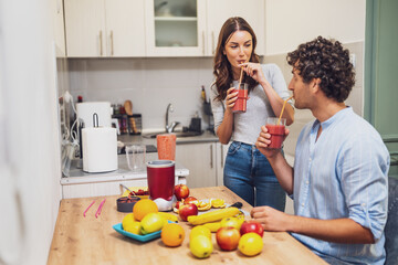 A couple enjoys freshly blended smoothies in their cozy kitchen, surrounded by colorful fruits and a blender filled with a vibrant mix.