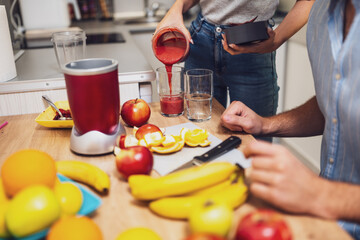 Close up of adult couple preparing smoothie in their kitchen. They are mixing various fruits in electric juicer.