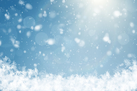Winter background with bright sunlight, soft falling snow, bokeh light effects, and frosty white snowflakes along the bottom against a clear blue sky