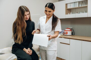 Professional cosmetologist consulting a female client about facial skincare in a beauty clinic