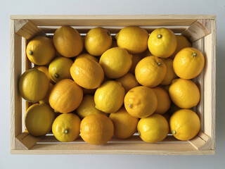 A wooden crate filled with fresh, ripe yellow lemons, viewed from directly above on a light background.