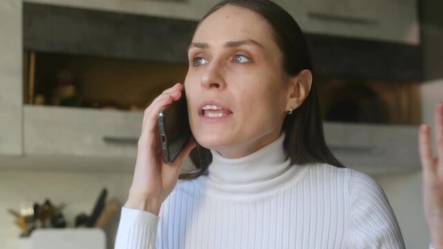 Annoyed woman emotionally arguing, gesturing during difficult phone call, expressing anger, frustration while talking on mobile phone in tense conversation at home. Angry woman arguing on smartphone