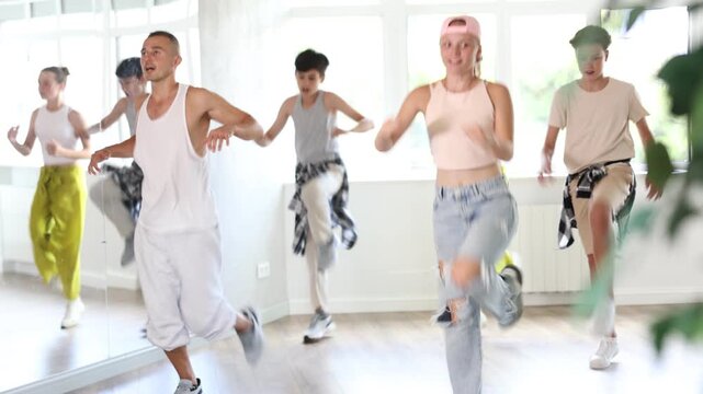 Happy teenage children and young male trainer practicing hip-hop reject steps during workout session in group. High quality 4k footage
