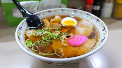 A close-up of a bowl of Japanese ramen, featuring sliced pork, half-boiled egg, scallions, bamboo shoots, and a pink swirl 
