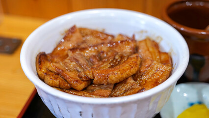 A close-up of a bowl filled with thick slices of glazed and grilled pork belly over rice (butadon), showing the rich color
