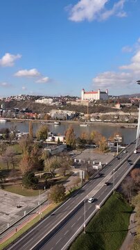 View of Bratislava city center with the historic castle on the hill and cars driving on the snp bridge across the danube river under a blue sky. 