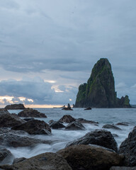 Naklejka premium Mystical seascape with dark volcanic rocks and tall sea stacks emerging from silky ocean water during twilight, show.casing serene coastal nature