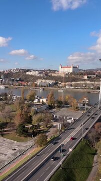 View of Bratislava city center with the historic castle on the hill and cars driving on the snp bridge across the danube river under a blue sky. 