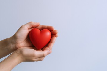 Fototapeta premium Hands gently holding red heart shape, symbolizing love, care, and health on a neutral background