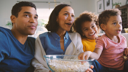 Family At Home Sitting On Sofa Watching TV And Eating Popcorn Together