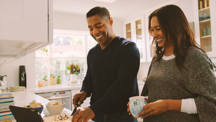 Mature Couple In Kitchen Preparing Meal With Man Following Online Recipe On Digital Tablet
