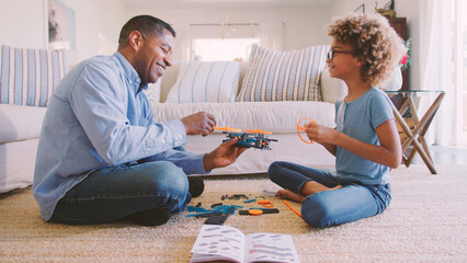 Grandfather And Granddaughter Sitting On Floor in Lounge At Home Building Construction Kit Together