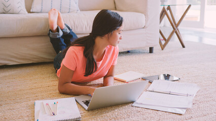 Young Girl Lying On Floor in Lounge At Home Doing Homework Using Laptop