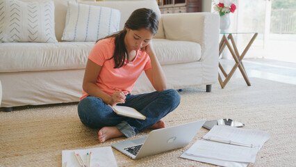 Young Girl Sitting On Floor in Lounge At Home Doing Homework Using Laptop