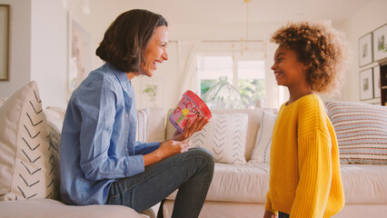 Daughter Giving Mother Plant Pot That She Has Decorated Herself Sitting On Sofa At Home