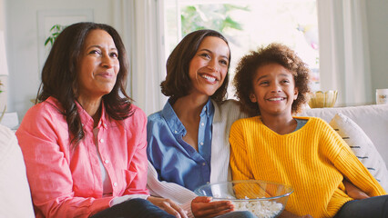 Female Multi Generation Family Sitting On Sofa At Home With Popcorn Watching TV Together